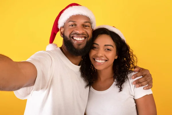 Aimer le couple afro-américain dans Santa chapeaux sourire et prendre selfie sur fond de studio jaune, espace libre — Photo