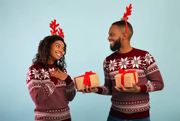 Чорний чоловік дарує різдвяний подарунок щасливій леді, святкуючи Різдво разом, стоячи на синьому фоні — стокове фото
