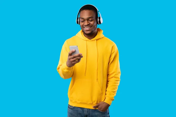 Africano en auriculares usando música de escucha de teléfonos inteligentes, fondo azul —  Fotos de Stock