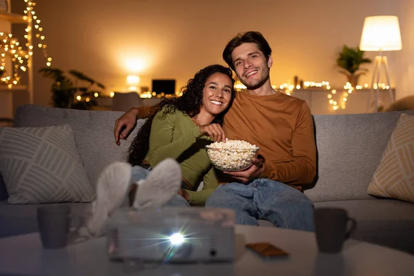 ホームシネマプロジェクターを使って映画を観る幸せなカップルが屋内に座って — ストック写真