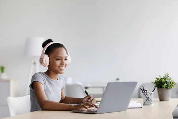 Allegro adolescente afro americano femmina in cuffie a studi tavolo al computer portatile a distanza — Foto Stock