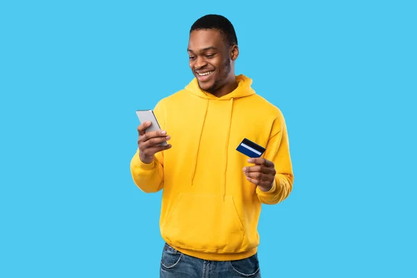 Hombre afroamericano usando tarjeta de crédito y teléfono celular, fondo azul —  Fotos de Stock