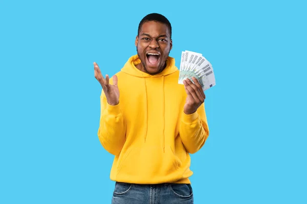 Emotionele zwarte man die schreeuwt met eurogeld over een blauwe achtergrond — Stockfoto