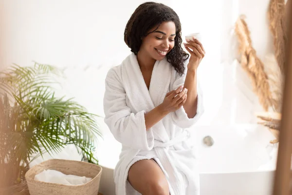 Afrikaanse vrouw hydraterende lichaam en handen aanbrengen van crème in de badkamer — Stockfoto
