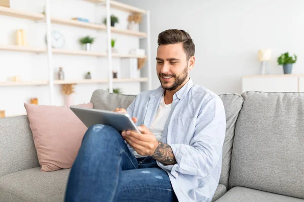 Entspannter Millennial-Mann ruht sich auf Sofa mit digitalem Tablet aus, surft in sozialen Netzwerken oder shoppt online, freier Platz — Stockfoto