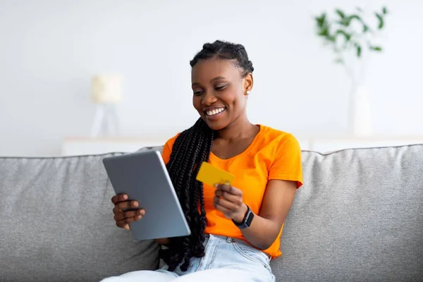 Fröhliche schwarze Frau, die online bezahlt, Waren im Internet kauft, Tablet und Kreditkarte zu Hause benutzt. Internet-Einkauf — Stockfoto