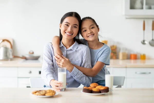 Szerető koreai anya és lánya élvezi a friss házi sütik, ivás tej, ül a konyhában belső — Stock Fotó