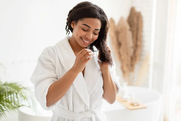 Negro hembra aplicando suero cuidado del cabello en el baño —  Fotos de Stock