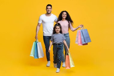 Alışveriş günü. Üç çocuklu neşeli Orta Doğulu bir aile alışveriş torbalarıyla yürüyor.