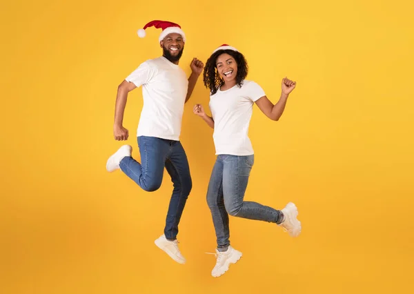 Kerstfeest. Positief zwart paar in santa hoeden springen in de lucht, plezier hebben, dansen en genieten van kerstvakantie — Stockfoto