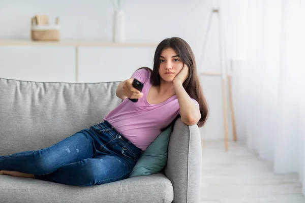 Annoiato adolescente indiano con telecomando guardare la TV sul divano a casa, spazio copia — Foto Stock