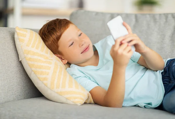 Счастливый мальчик лежит на диване, используя смартфон — стоковое фото