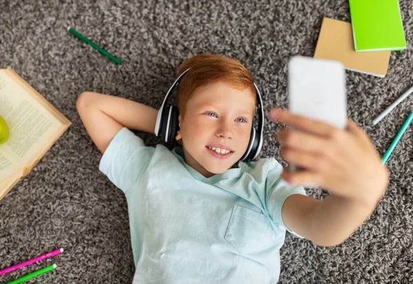 Schattig kind met behulp van headset en mobiele telefoon tijdens het doen van huiswerk — Stockfoto