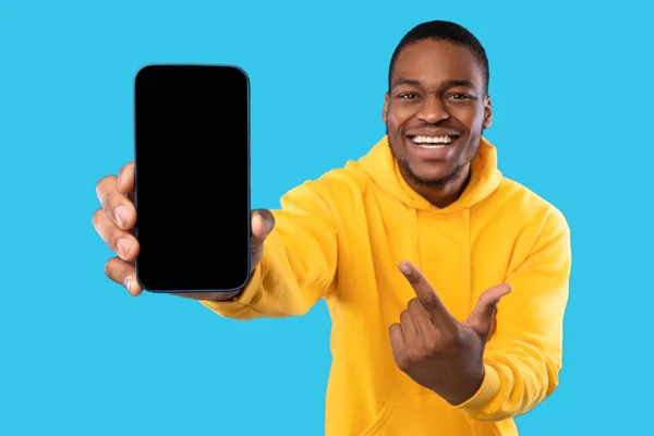Afrikaner zeigt Handy mit leerem Bildschirm vor blauem Hintergrund — Stockfoto