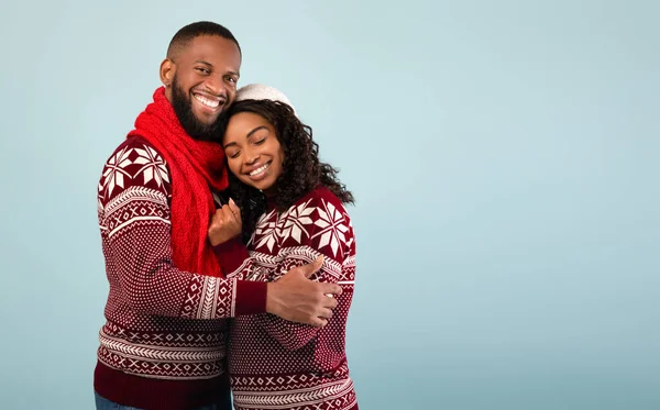 Pasangan african american african dalam sweater Natal merangkul, berdiri di atas latar belakang biru, ruang kosong — Stok Foto