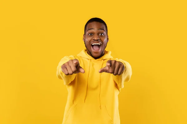 Heyecanlı Afrikalı Amerikalı adam parmaklarını kameraya doğrultuyor, sarı arka plan — Stok fotoğraf