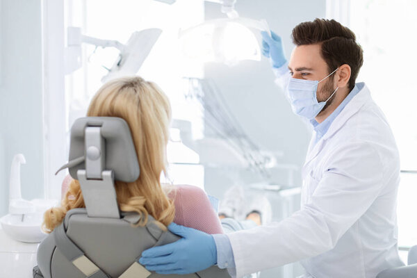 Male dentist in face mask greeting blonde woman patient