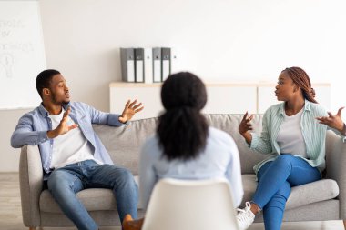 Siyahi evli çift, fizyolog ofisinde tartışırken aile içi çatışmaları çözmek için profesyonel yardım alıyorlar.