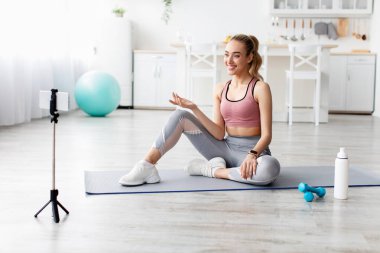 Gülümseyen Avrupalı güzel milenyum sarışın fitness blogcusu kadın webcam 'e bakıyor ve egzersiz yapıyor