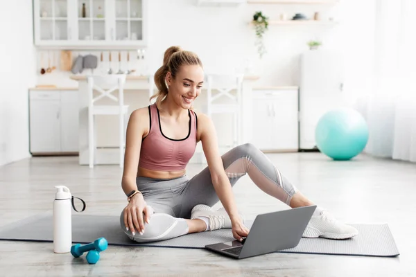 Allegro caucasico abbastanza millenario bionda fitness blogger femminile guardando il computer portatile, allenatore chat e scegliere on-line lezione di allenamento — Foto Stock