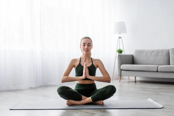 Feliz calma europea bonita joven rubia practicando yoga, sentada en posición de loto con los ojos cerrados —  Fotos de Stock