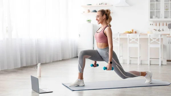 Nöjd europeisk ganska ung blond fitness kvinna gör övningar med hantlar och titta på online träning — Stockfoto