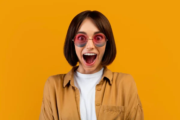 Verrast jonge vrouw in kleurrijke zonnebril schreeuwen WOW, opening mond in opwinding over gele achtergrond — Stockfoto