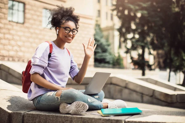 Negro estudiante chica con portátil ondeando mano sentado fuera — Foto de Stock