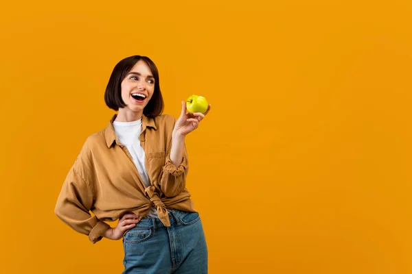 Βιταμίνες για υγιή και δυνατά δόντια. Θετική κυρία που κρατάει το ώριμο πράσινο μήλο και βλέπει στην άκρη τον ελεύθερο χώρο — Φωτογραφία Αρχείου