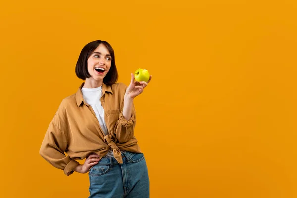 Vitaminas para dentes saudáveis e fortes. Senhora positiva segurando maçã verde madura e olhando para o espaço livre — Fotografia de Stock