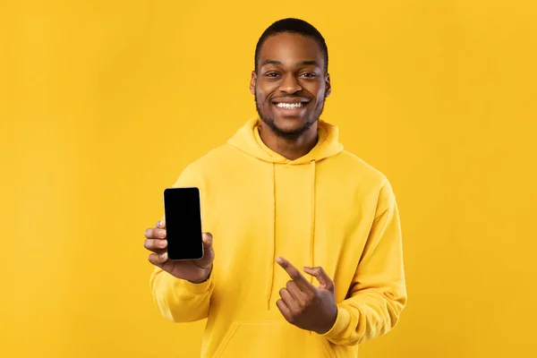 Preto homem mostrando telefone apontando dedo na tela, fundo amarelo — Fotografia de Stock