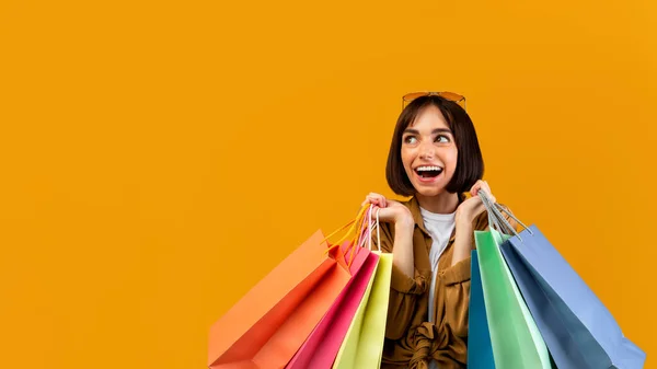 Señora emocionada con bolsas de compras sonriendo y mirando el espacio libre, ofreciendo lugar para su anuncio sobre fondo amarillo — Foto de Stock