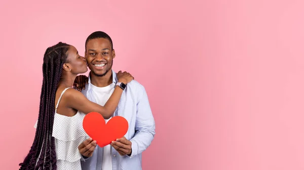 Joven romántico negro pareja besos y celebración rojo papel corazón — Foto de Stock