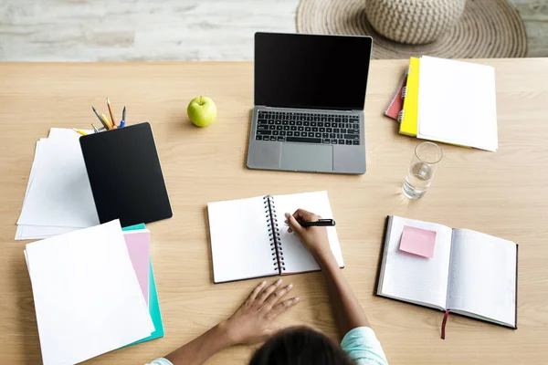 Adolescente afroamericana niña estudiante escribiendo en el cuaderno en el escritorio con el ordenador portátil con pantalla en blanco y estudios — Foto de Stock