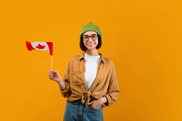 Nowoczesna koncepcja edukacji zagranicznej. Happy uczennica wymiany posiadający małą flagę Kanady, żółte tło — Zdjęcie stockowe