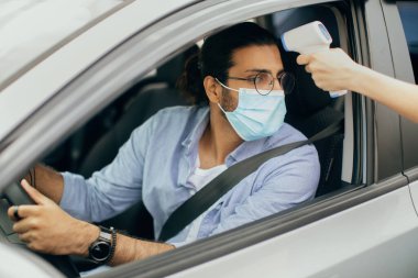 Hintli sürücü koruyucu yüz maskesi takıyor, sıcaklık kontrolü yaptırıyor.