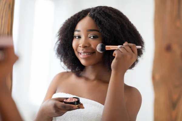 Konsep riasan alami. Wanita kulit hitam yang menawan mengenakan blusher atau bubuk di depan cermin di rumah — Stok Foto