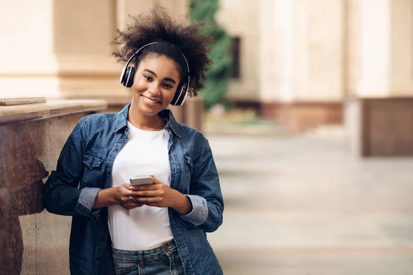 Счастливая африканская студентка пользуется мобильным телефоном в наушниках — стоковое фото