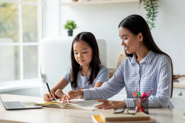 Jonge aziatische moeder helpen haar dochter met huiswerk, zitten aan het bureau in keuken interieur, vrije ruimte — Stockfoto