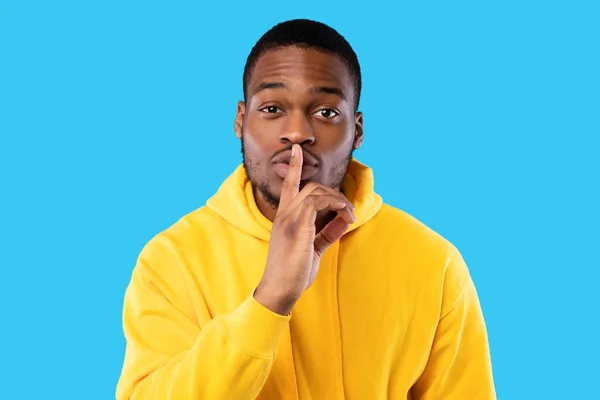 Black man gesturing finger-on-lips sign looking at camera, blue background — Stock Photo, Image