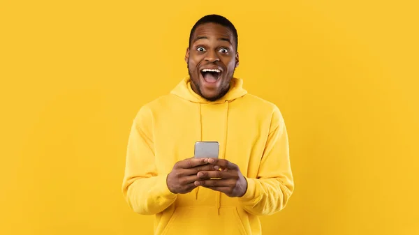 興奮アフリカ系アメリカ人の男は黄色の背景にスマートフォンを保持 — ストック写真