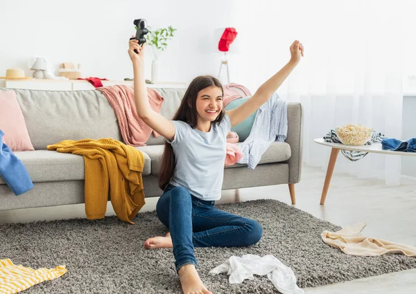Indiaas tiener meisje spelen video games met joystick, zitten op de vloer en het verhogen van de handen, vieren van de overwinning thuis — Stockfoto