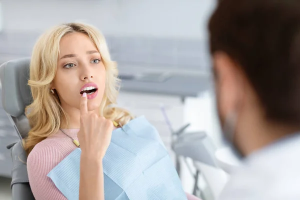 Diş kliniğini ziyaret eden çekici sarışın kadın, dişini işaret ediyor. — Stok fotoğraf