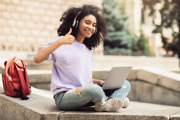 Afroamericana estudiante chica usando portátil gestos pulgares-up aprendizaje al aire libre — Foto de Stock