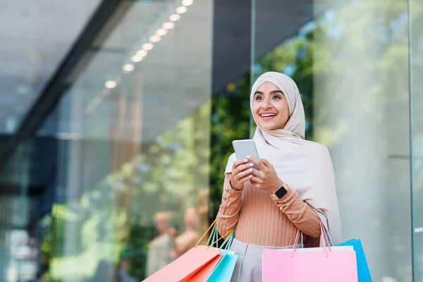 Sorprendido sonriendo lindo joven árabe musulmán hembra en hijab disfruta de la venta con muchos paquetes y mensajes de texto mensaje — Foto de Stock