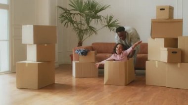 Genç, Afro-Amerikan babası içinde küçük kızı olan karton kutuları itiyor, kız yeni evinde eğleniyor.