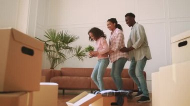 Üç kişilik mutlu Afro-Amerikan ailesi, yeni dairesindeki karton kutuların arasında yerli bitkilerle dans ediyor.
