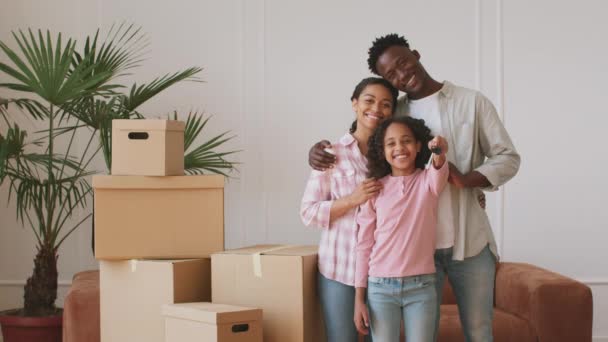 Glückliche junge afrikanisch-amerikanische Familie mit Eltern und kleiner Tochter zeigt Schlüssel zur Kamera, posiert in der eigenen Wohnung — Stockvideo