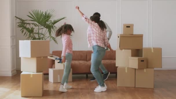 Щасливі афроамериканські батьки й дочка танцюють у новій квартирі серед багатьох картонних ящиків, насолоджуючись мандрівним днем. — стокове відео