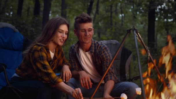 Conceito de acampamento e piquenique. Jovem carinhoso homem e mulher fritando marshmallow em chamas, desfrutando de noite na floresta — Vídeo de Stock